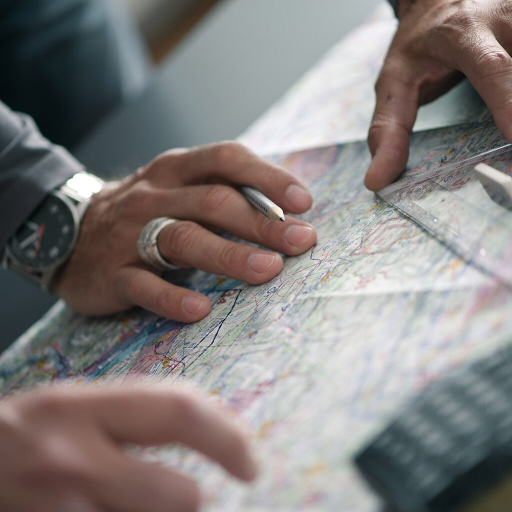 Hände auf einer Karte bei der Flugplanung im kayfly Hangar im Rahmen der Ausbildung zur Pilotenlizenz für Helikopter